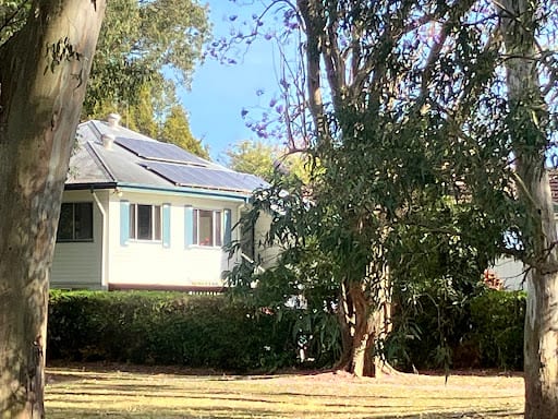 Solar panels installed on roof of white residential home surrounded by trees.
